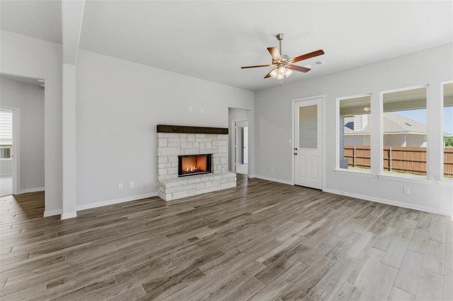 Unfurnished living room with ceiling fan, a stone fireplace, and light wood-style flooring