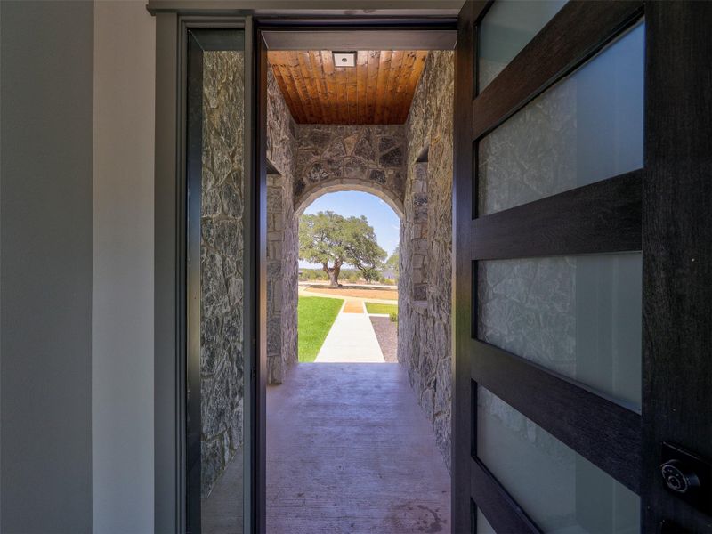 An arched stone breezeway framing the front yard pathway welcomes guests with rustic charm.