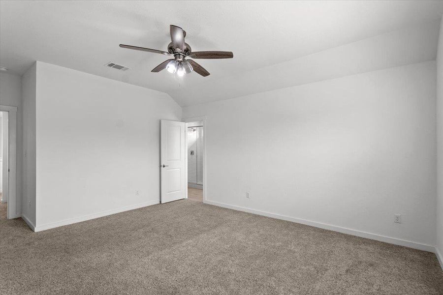 A spacious bedroom offers a neutral palette, plush carpeting, and a modern ceiling fan for comfort.