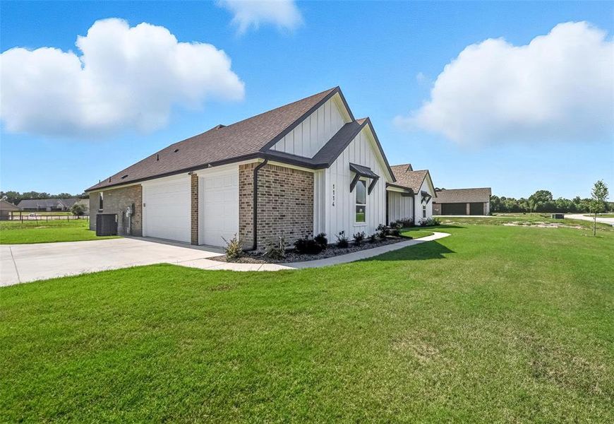 View of home's exterior featuring board and batten siding, a lawn, concrete driveway, and brick siding View of home's exterior featuring board and batten siding, a lawn, concrete driveway, and brick siding