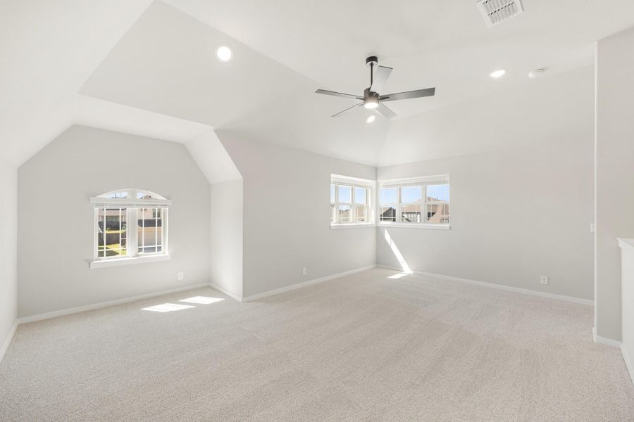 Large empty bedroom with vaulted ceiling, ceiling fan, carpet flooring, and two windows