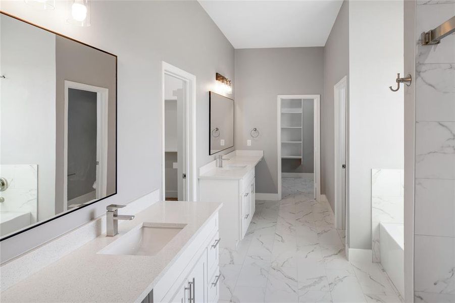 Full bath with a tub with marble appearance, two vanities, a spacious closet, and light marble finish floors Full bath with a tub with marble appearance, two vanities, a spacious closet, and light marble finish floors