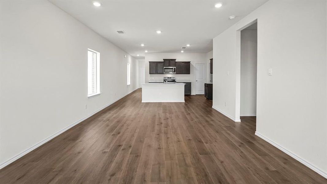 This expansive living area features wide plank flooring, recessed lighting, and bright white walls