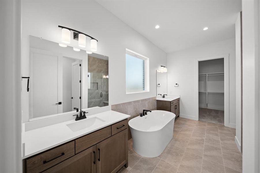 Bathroom with two vanities, a walk in closet, a freestanding bath, a stall shower, and light tile patterned flooring