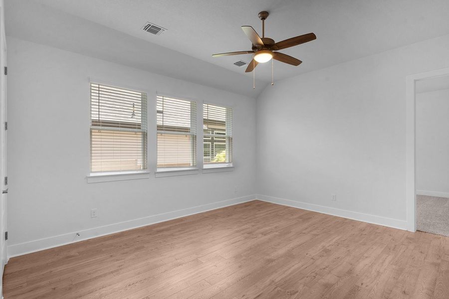 A well-lit bedroom features hardwood flooring and ample natural light from three large windows.