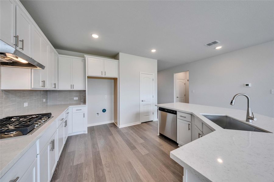 Kitchen with a sink, stainless steel appliances, light wood-style flooring, white cabinets, and tasteful backsplash Kitchen with a sink, stainless steel appliances, light wood-style flooring, white cabinets, and tasteful backsplash