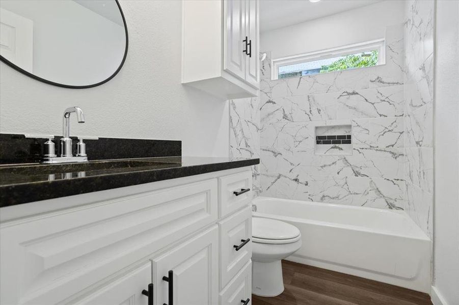 Full bathroom with vanity, tiled shower / bath combo, toilet, and hardwood / wood-style flooring