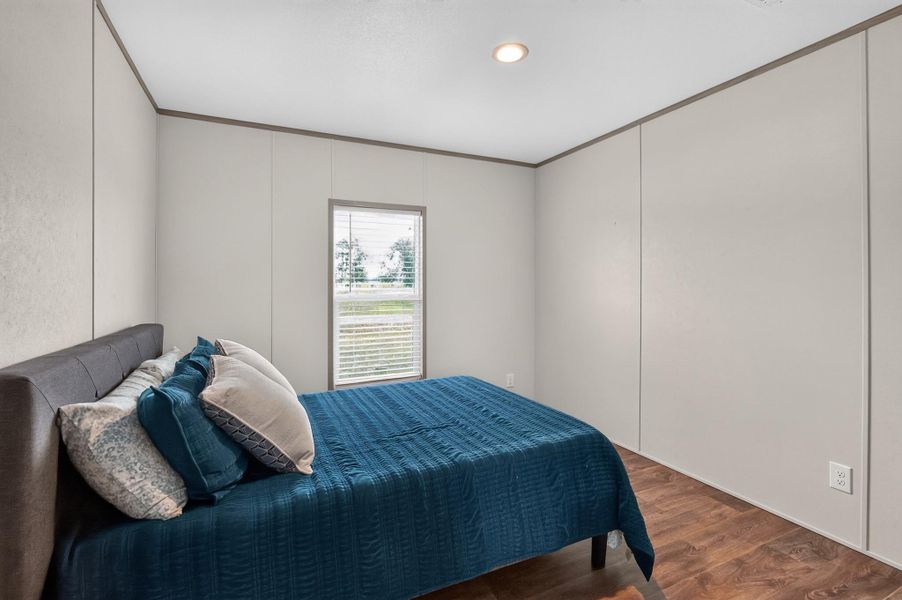 A quiet bedroom retreat features ample natural light from a well-placed window, complementing the rich wood flooring.