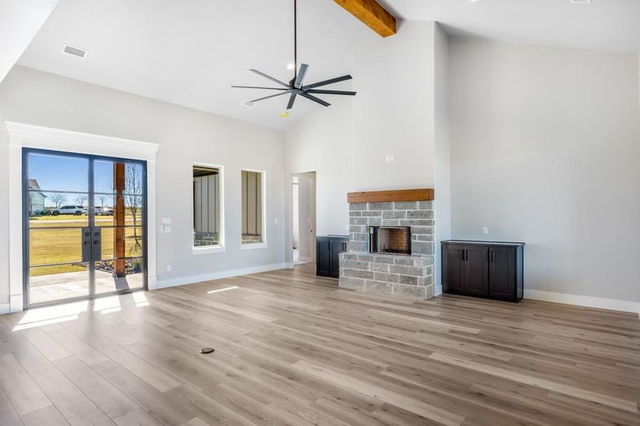 Unfurnished living room featuring high vaulted ceiling, a stone fireplace, ceiling fan, light hardwood / wood-style floors, and beam ceiling