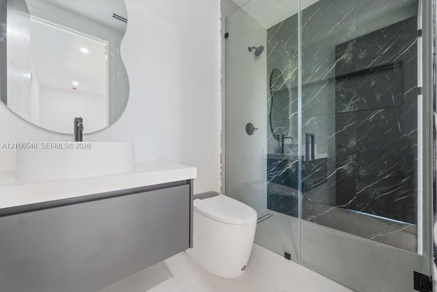 Floating vanity with a white vessel sink, dark stone-finish shower surround, glass shower enclosure, and organic-shaped wall mirror