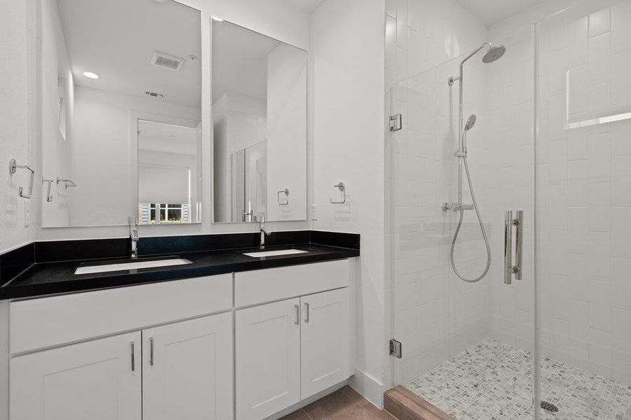 Dual vanity with dark counters and modern fixtures complements the sleek glass-enclosed shower with subway tile. Dual vanity with dark counters and modern fixtures complements the sleek glass-enclosed shower with subway tile.