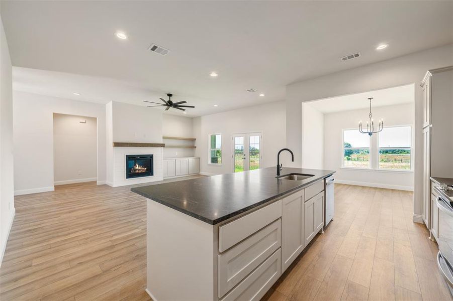 Kitchen with dishwasher, an island with sink, dark countertops, ceiling fan, and light wood-type flooring
