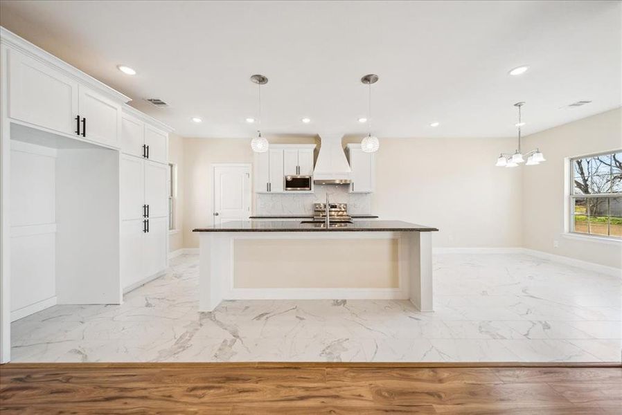 Kitchen featuring decorative light fixtures, white cabinetry, stainless steel microwave, and premium range hood