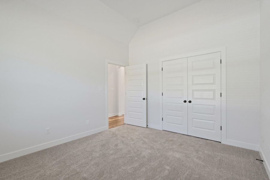 Vaulted ceiling, plush carpet flooring, white walls, white paneled doors, and black door hardware Vaulted ceiling, plush carpet flooring, white walls, white paneled doors, and black door hardware