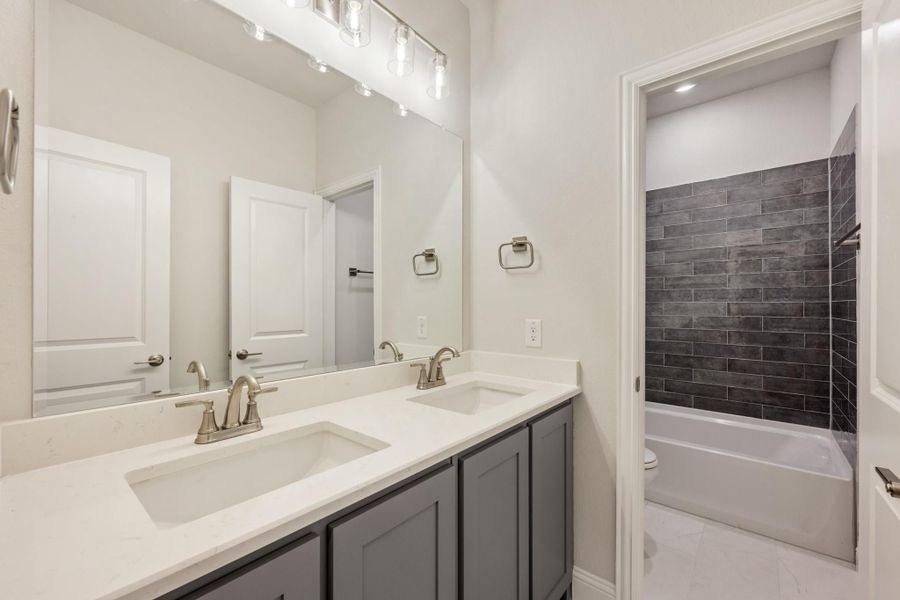 Bathroom with double sink vanity, gray cabinets, white countertop, and tub with dark tile surround Bathroom with double sink vanity, gray cabinets, white countertop, and tub with dark tile surround