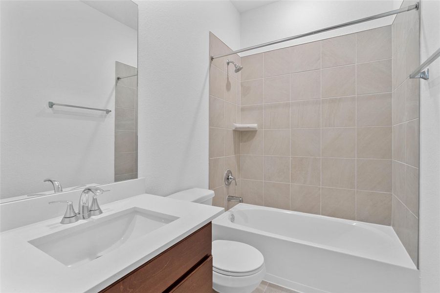The secondary bathroom showcases tile flooring, a bath/shower combo with tile surround, a vanity with a stunning light countertop, a mirror, sleek fixtures, and contemporary finishes throughout.