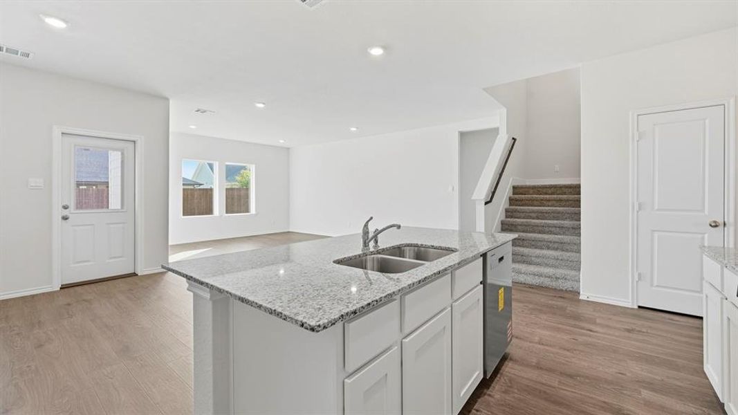 Kitchen with white cabinets, light stone counters, light wood-style floors, an island with sink, and open floor plan