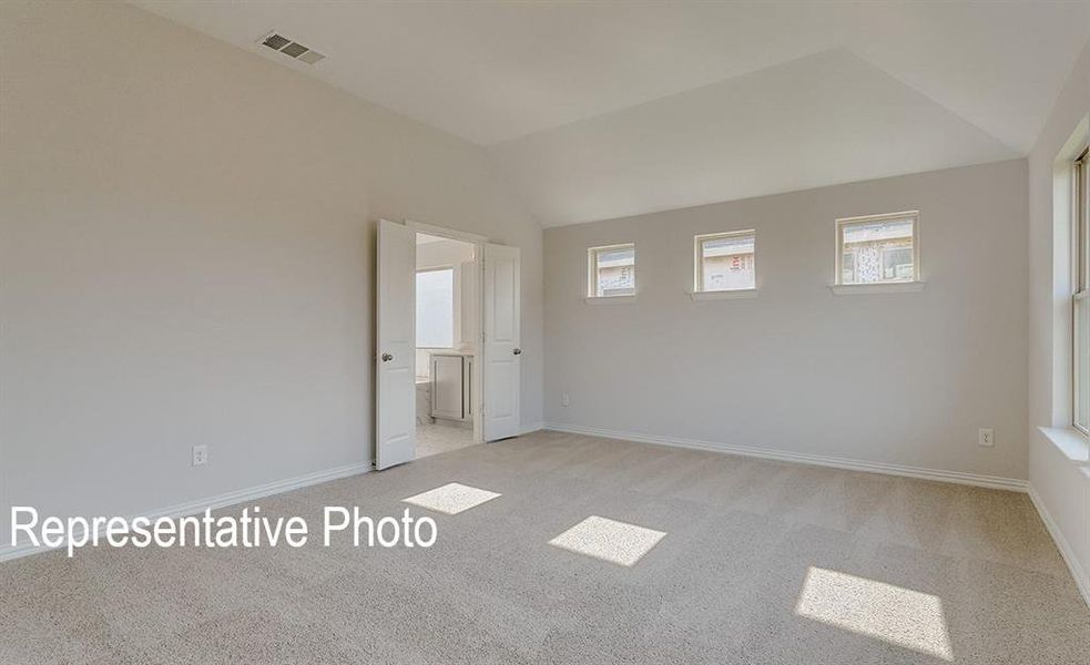Spacious room featuring vaulted ceilings, light-colored carpeting, multiple windows for ample natural light, and double doors opening to an adjacent tiled space