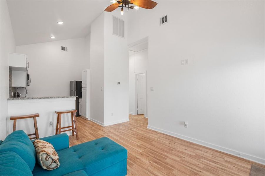 This is another view of the modern living space with high ceilings,  and a kitchen bar area. The room has a clean, minimalist feel with plenty of natural light.