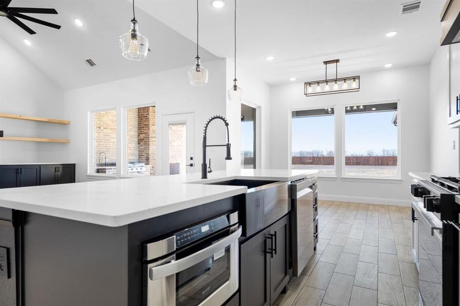 Kitchen featuring stainless steel oven, decorative light fixtures, an island with sink, and stove