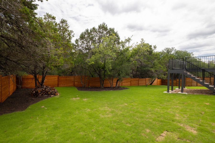 A well-maintained lawn with mature trees borders a newly installed wooden fence, offering a verdant retreat.