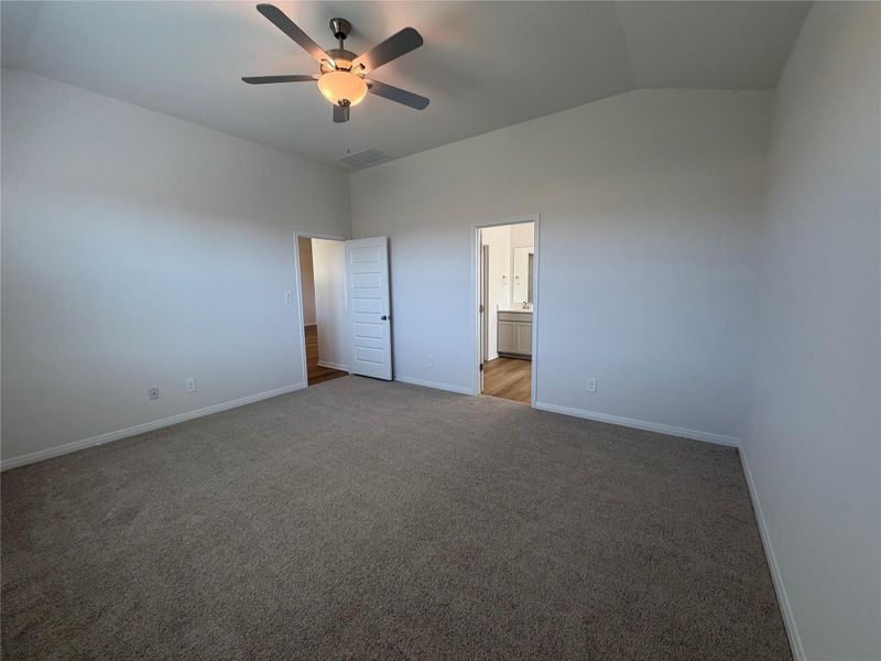 Unfurnished bedroom with vaulted ceiling, a ceiling fan, carpet, and connected bathroom Unfurnished bedroom with vaulted ceiling, a ceiling fan, carpet, and connected bathroom