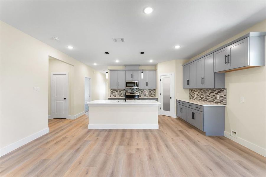 Kitchen with stainless steel appliances, gray cabinetry, and decorative light fixtures