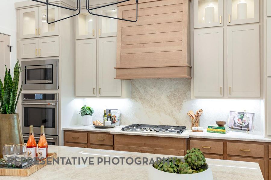 Kitchen featuring hanging light fixtures, tasteful backsplash, glass insert cabinets, appliances with stainless steel finishes, and premium range hood Kitchen featuring hanging light fixtures, tasteful backsplash, glass insert cabinets, appliances with stainless steel finishes, and premium range hood