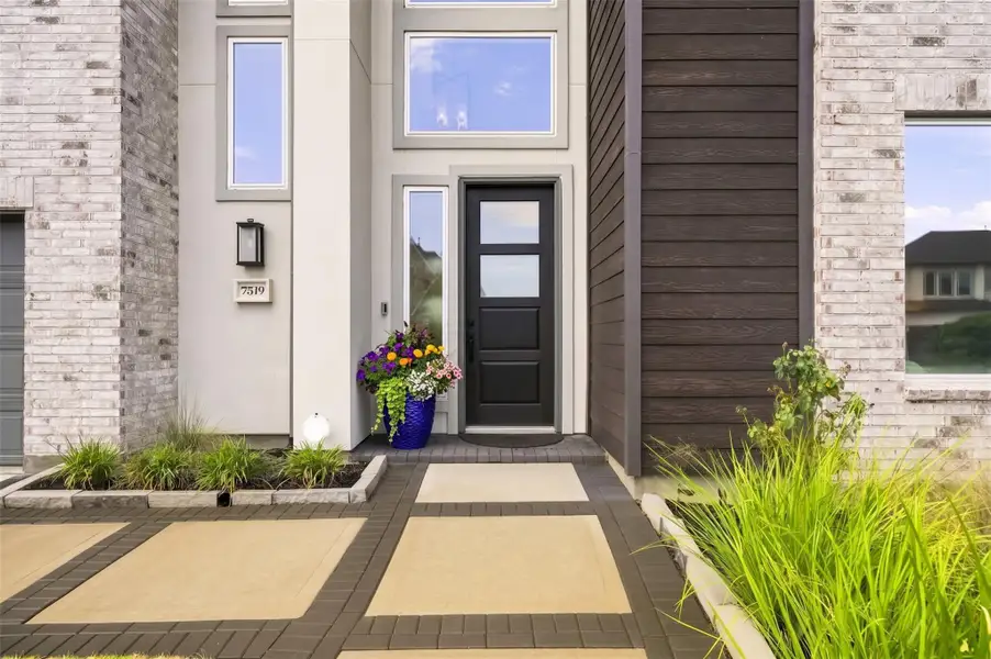 Arrive home to a sophisticated modern exterior where rich brick, warm wood accents, and sleek stucco create a striking architectural presence. Professionally designed landscaping enhances the curb appeal, while a wide brick-paver walkway leads to the entrance with an elegant, estate-like feel.