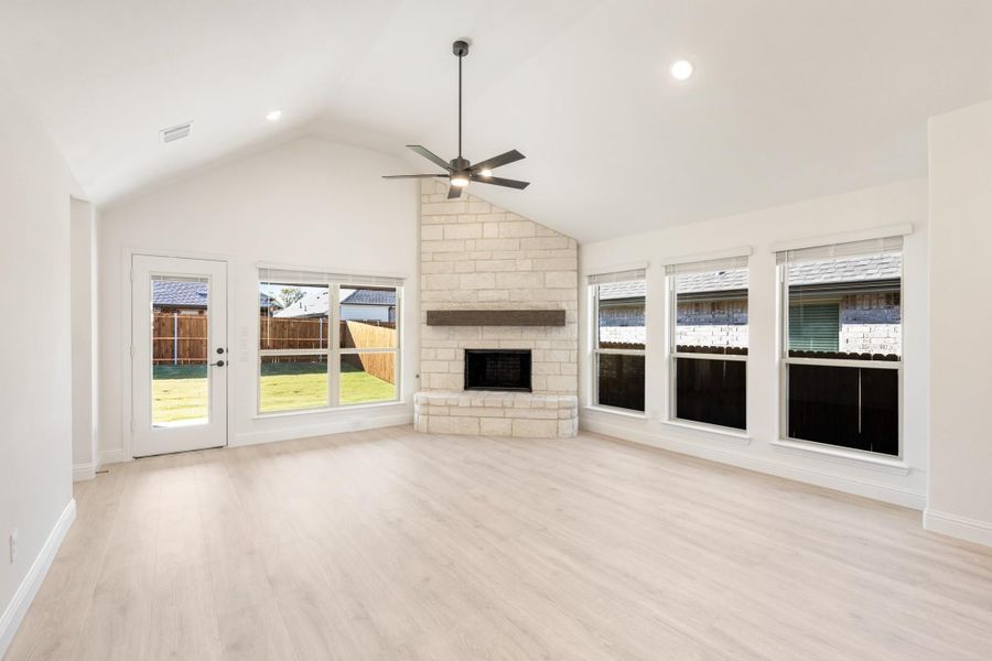 Open living room with vaulted ceiling, stone fireplace, ceiling fan, and light hardwood floors