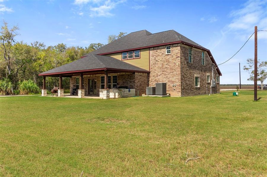 This spacious brick house features a large, covered patio perfect for outdoor living. It's set on a generous lawn with a scenic, wooded backdrop, offering both privacy and tranquility.