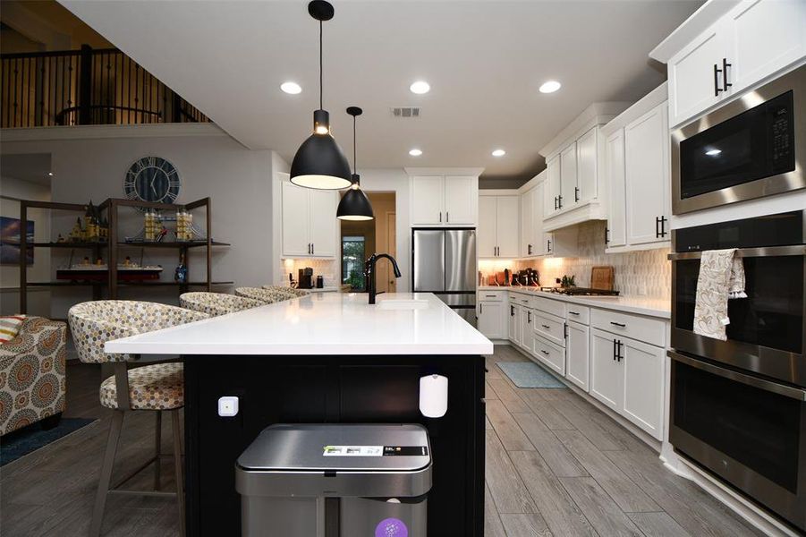 This modern kitchen features sleek white cabinetry, stainless steel appliances, and a large island with pendant lighting. The open layout flows into a cozy seating area, perfect for entertaining. The space is bright and inviting, with ample countertop space and contemporary finishes.