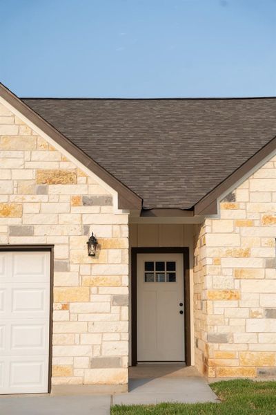 View of exterior entry with a shingled roof, stone siding, and a garage