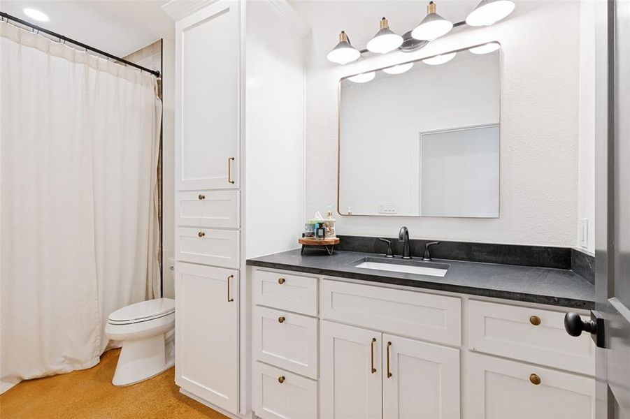 Bathroom featuring a white vanity with dark countertop, undermount sink, and black faucet Bathroom featuring a white vanity with dark countertop, undermount sink, and black faucet