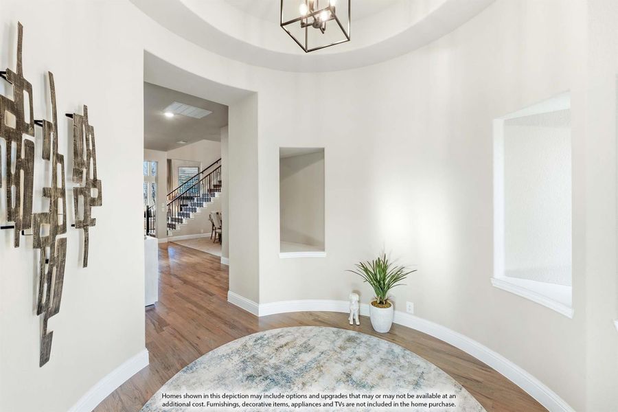 Curved foyer with tray ceiling, pendant light, hardwood floors, and staircase visible in background Curved foyer with tray ceiling, pendant light, hardwood floors, and staircase visible in background