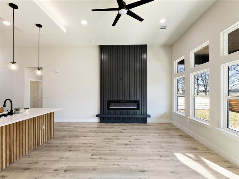 Unfurnished living room with a glass covered fireplace, ceiling fan, light wood-type flooring, recessed lighting, and a high ceiling