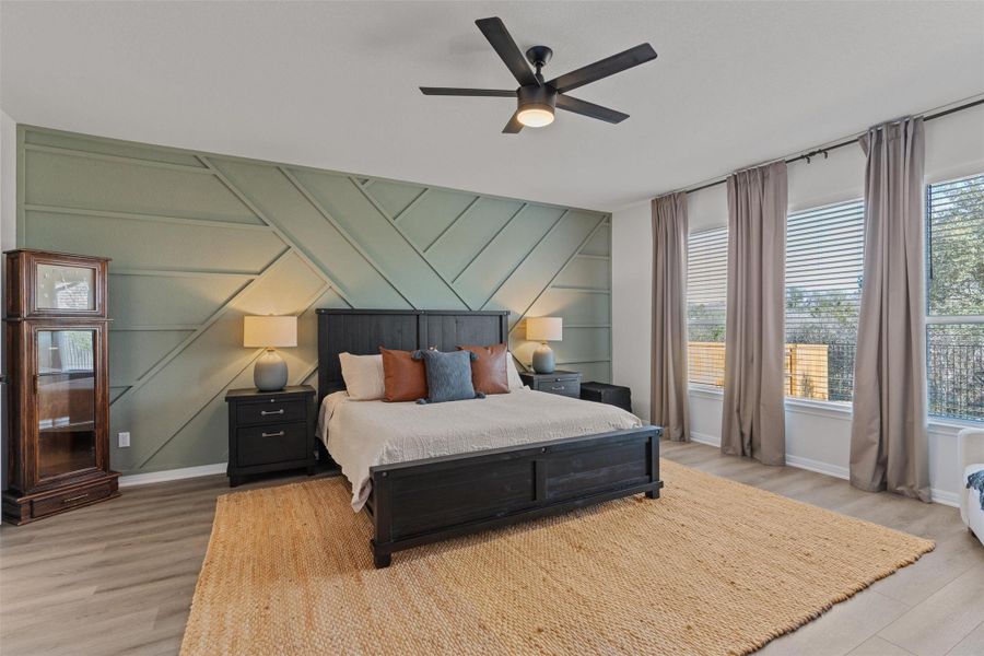 Bedroom with an accent wall, a decorative wall, light wood-style floors, and a ceiling fan