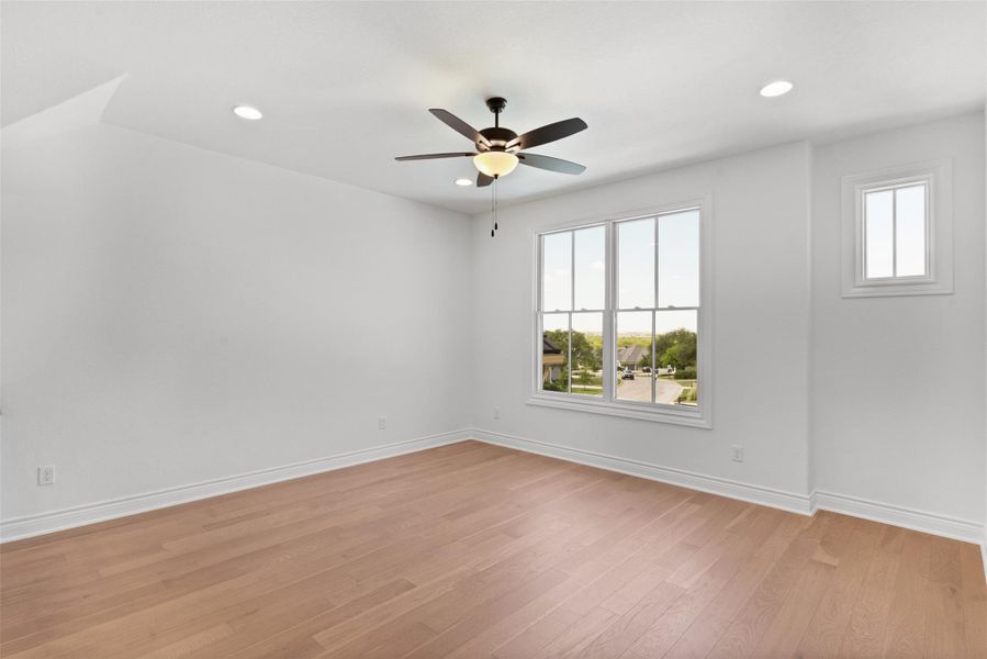 This room features light hardwood flooring, white walls, and a ceiling fan with integrated lighting
