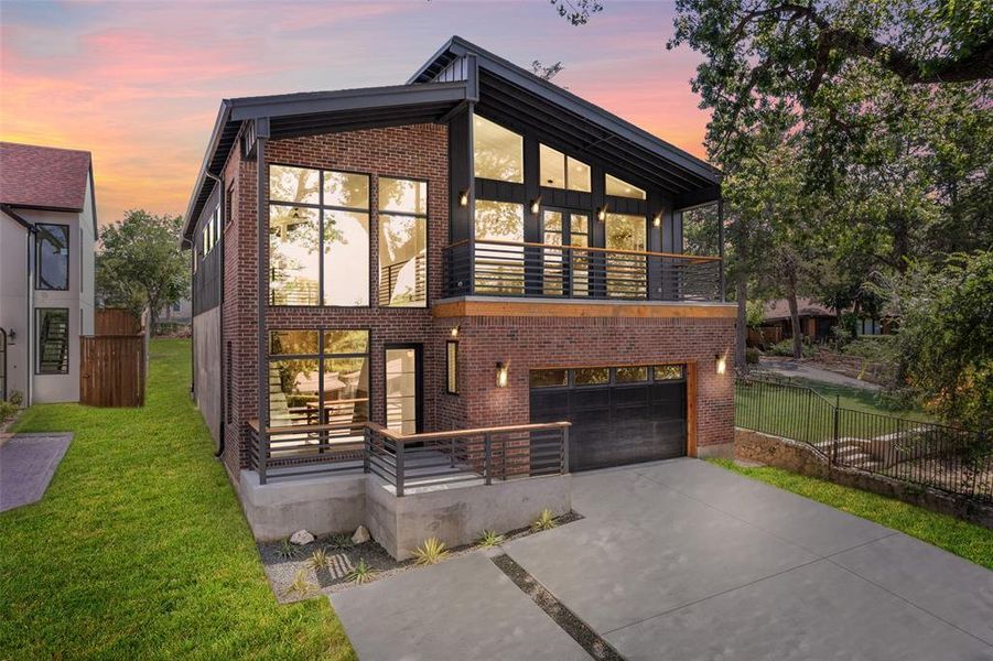 Contemporary house featuring a balcony, driveway, brick siding, and an attached garage