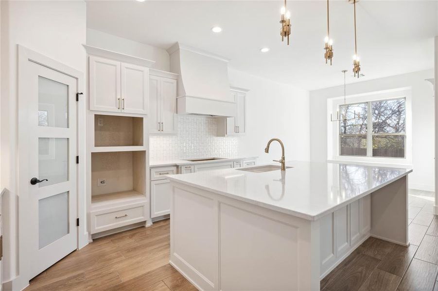 Kitchen featuring white cabinets, custom exhaust hood, hanging light fixtures, and sink