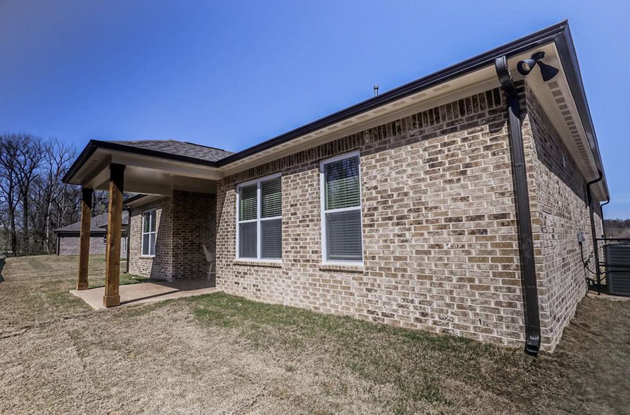 Brick exterior featuring a covered patio with wood columns, white window frames, and dark gutters