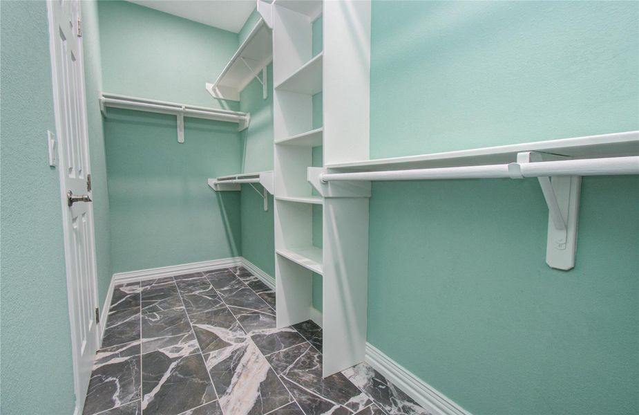 This photo showcases a spacious walk-in closet with teal walls and elegant marble-patterned flooring. It features ample shelving and hanging space, providing excellent storage solutions.