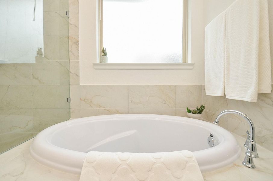 A luxurious oval soaking tub with elegant marble tiles and a modern glass shower enclosure with soft natural light filtering through a frosted window.