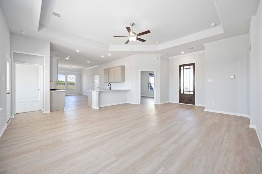 Open-concept living room and kitchen with light wood floors and tray ceiling