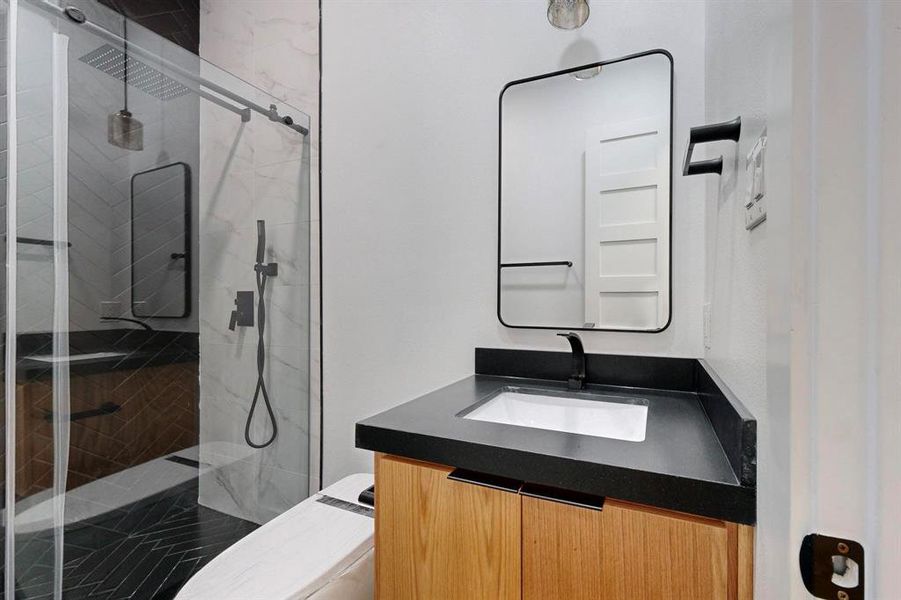 Modern bathroom featuring a wood-finish vanity with a black countertop, a rectangular undermount sink, and a black-framed mirror Modern bathroom featuring a wood-finish vanity with a black countertop, a rectangular undermount sink, and a black-framed mirror