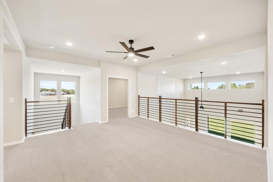 Open upstairs loft with carpet flooring, ceiling fan, and modern metal railing overlooking lower level Open upstairs loft with carpet flooring, ceiling fan, and modern metal railing overlooking lower level