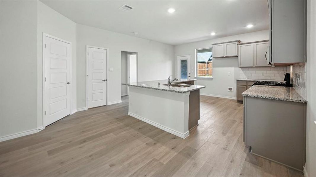 Kitchen with light stone counters, gas range oven, a kitchen island with sink, backsplash, and recessed lighting Kitchen with light stone counters, gas range oven, a kitchen island with sink, backsplash, and recessed lighting