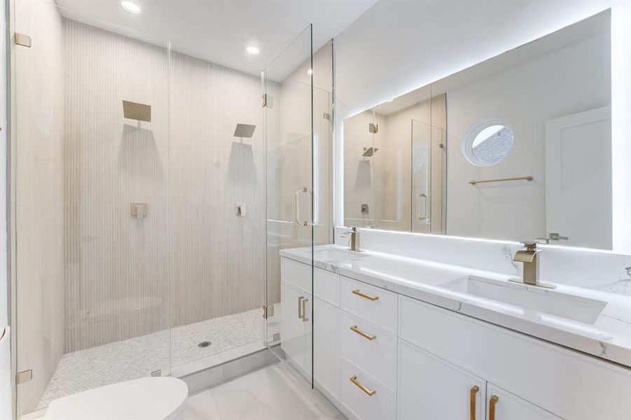 The primary suite features a light frameless mirror, double sinks, gold hardware, and chic white cabinetry for storage.