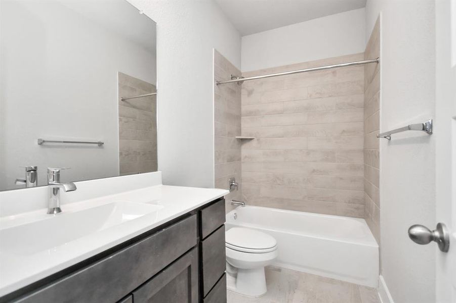 Experience sophistication in the secondary bathroom, where tile flooring complements a bath/shower combo with tile surround. Dark wood cabinets complete with a beautiful light countertop, enhances the space for a truly inviting ambiance. Sample photo of completed home. Actual colors and selections will vary.