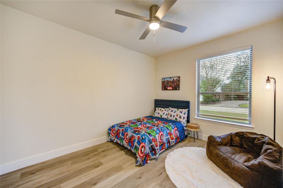 This cozy bedroom includes a ceiling fan, a large window providing ample natural light, The wood flooring creating a welcoming space.